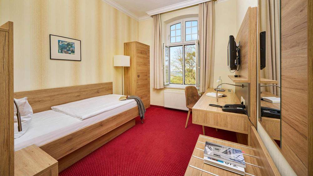 Einzelzimmer im Strandhotel Kormoran mit Schreibtisch, Spiegel, Fernseher und Fenster mit Blick zur Ostsee.