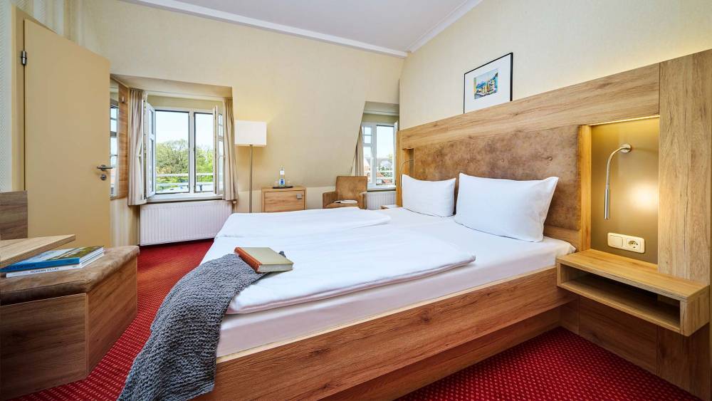 Doppelzimmer im Strandhotel Kormoran mit Ostseeblick, großem Bett, Schreibtisch, Sessel und Nachttischlampen.