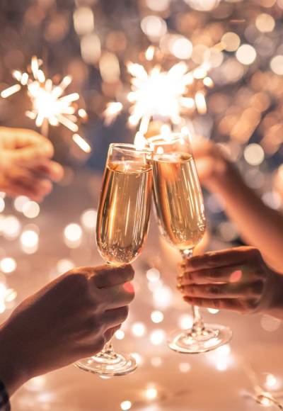 Zwei Personen halten an Silvester Gläser und Wunderkerzen in den Händen und stoßen auf das neue Jahr an.