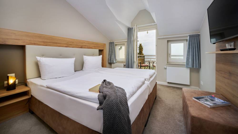 Schlafzimmer mit Doppelbett, TV und Balkonzugang in der Juniorsuite mit Panorama-Meerblick auf Usedom.