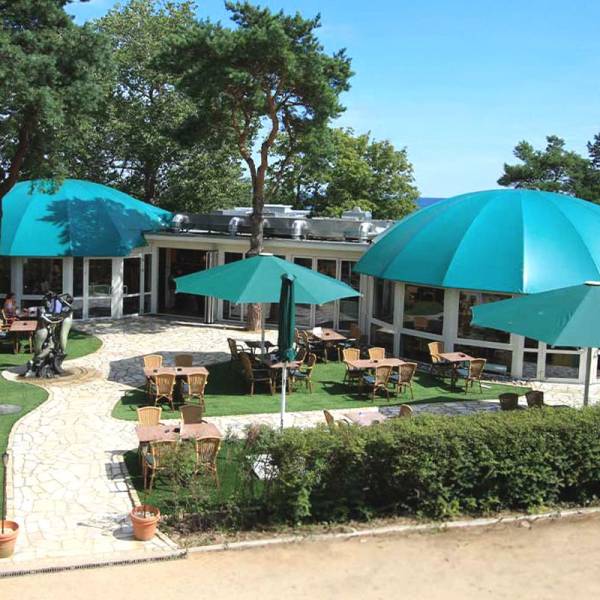 Sommerliches Promenadenrestaurant von Schöner Inseln mit türkisfarbenen Kuppeln und Sitzplätzen unter Pinien am Meer.