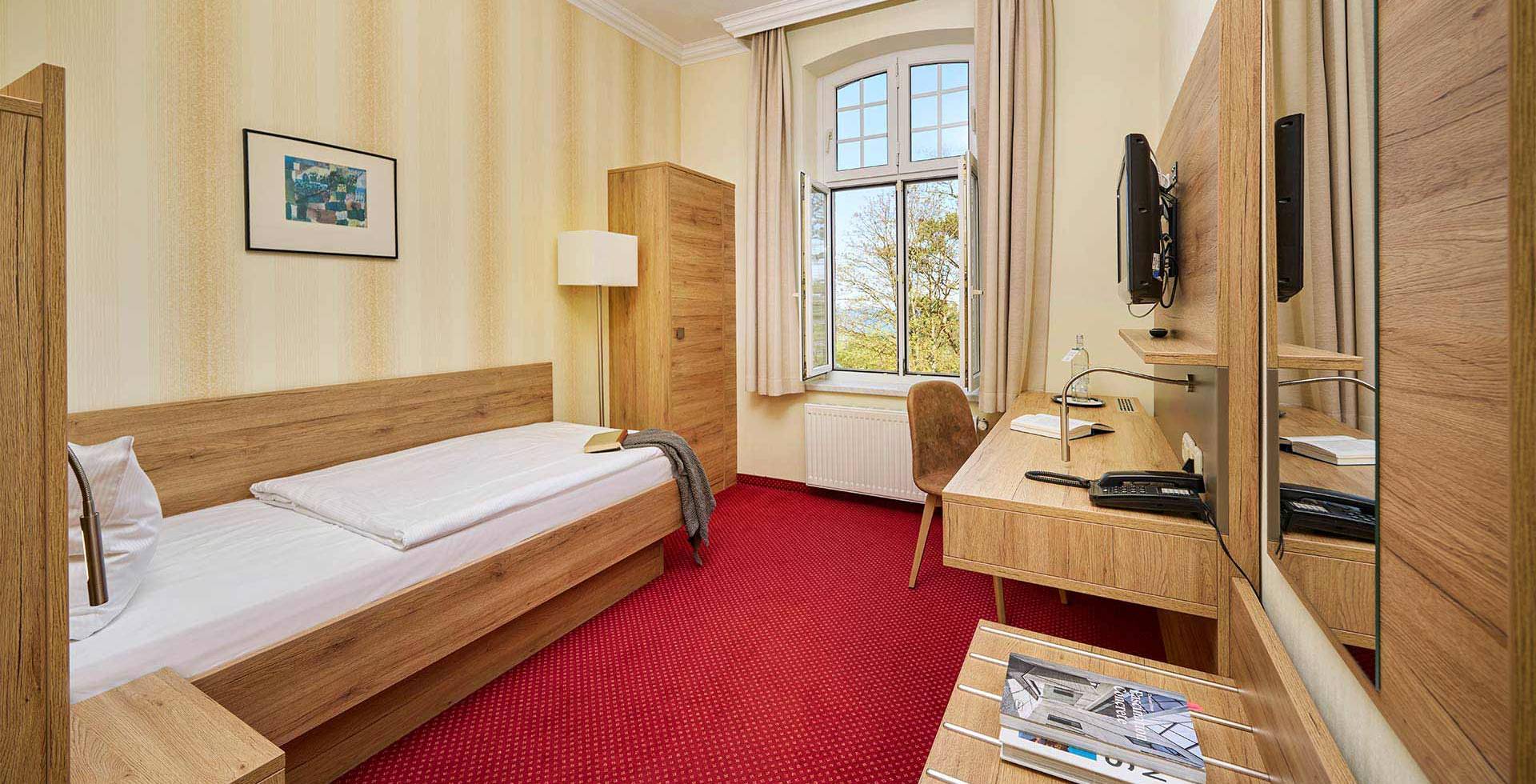 Einzelzimmer im Strandhotel Kormoran mit Schreibtisch, Spiegel, Fernseher und Fenster mit Blick zur Ostsee.