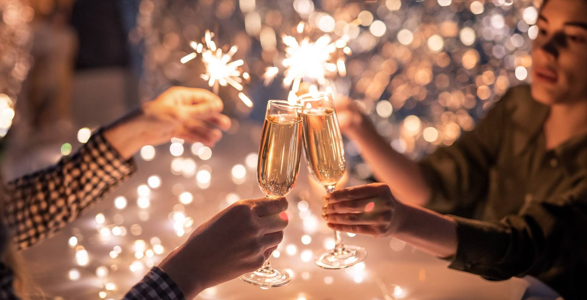 Zwei Personen halten an Silvester Gläser und Wunderkerzen in den Händen und stoßen auf das neue Jahr an.