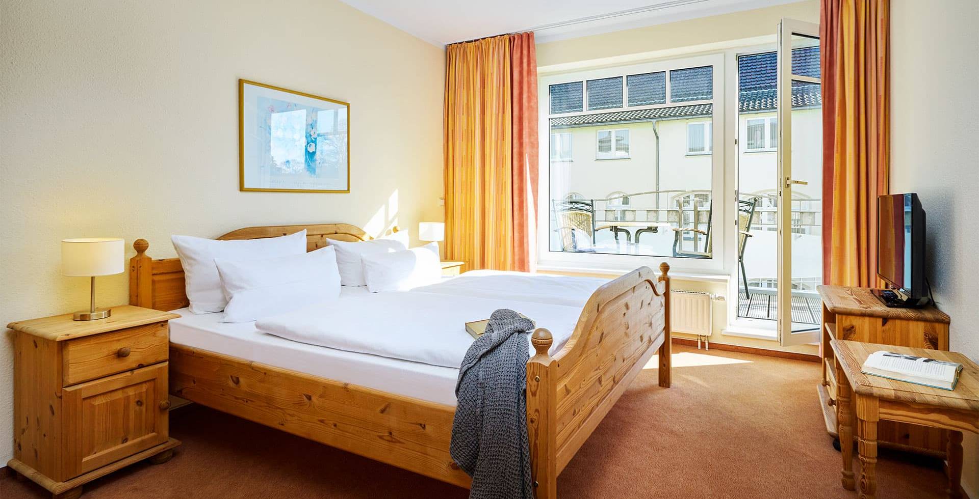 Helles Schlafzimmer mit Doppelbett, Nachttischen, Fernseher und Zugang zum Balkon im Strandhotel Luise in Zinnowitz.