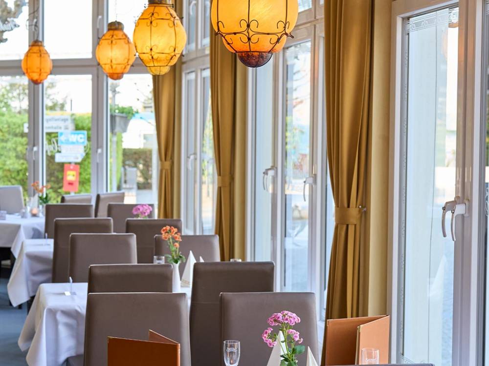 Restaurantbereich des Restaurants Lineti mit modernen Stühlen, weißen Tischdecken, Blumen und Blick nach draußen auf Usedom.