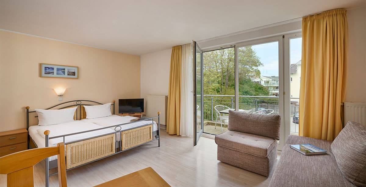 Moderne Einrichtung eines Zimmers im Appartement-Hotel Haus Strandperle mit Sofa, Doppelbett und Balkon.