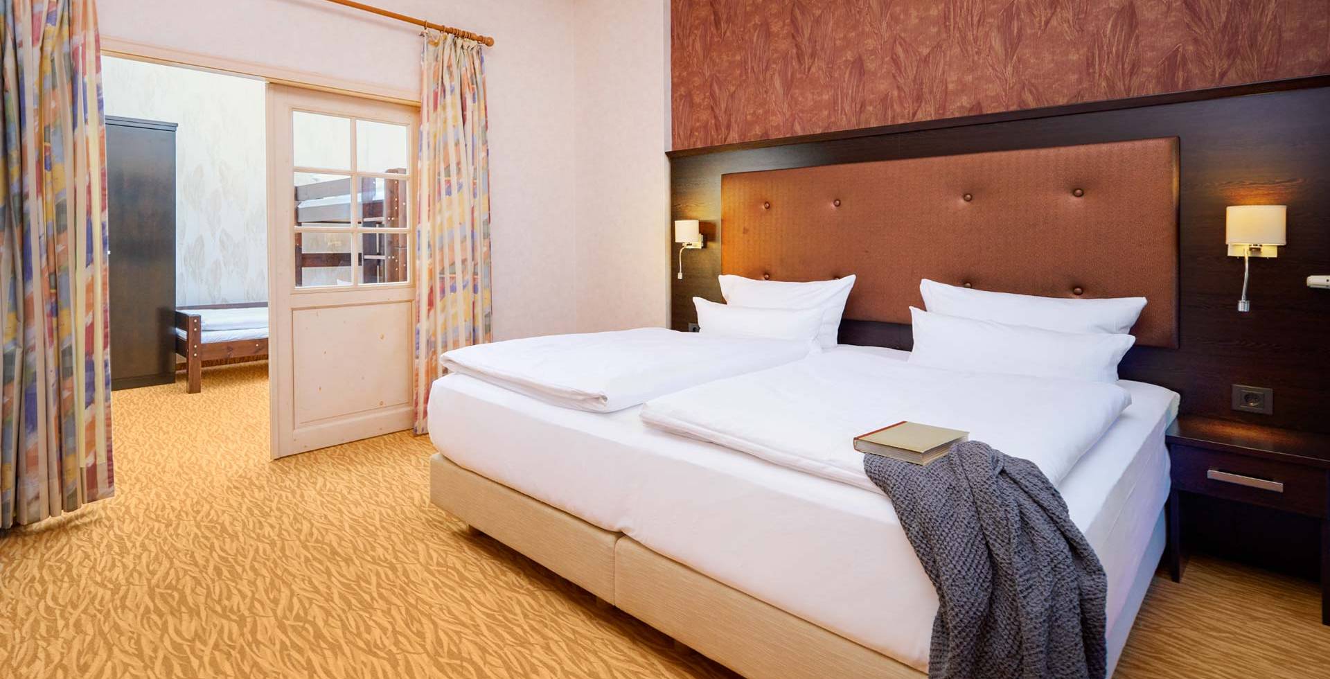 Doppelbett mit Nachttischen, Lampen und Blick ins Kinderzimmer der Family Suite im Hotel Preußenhof.