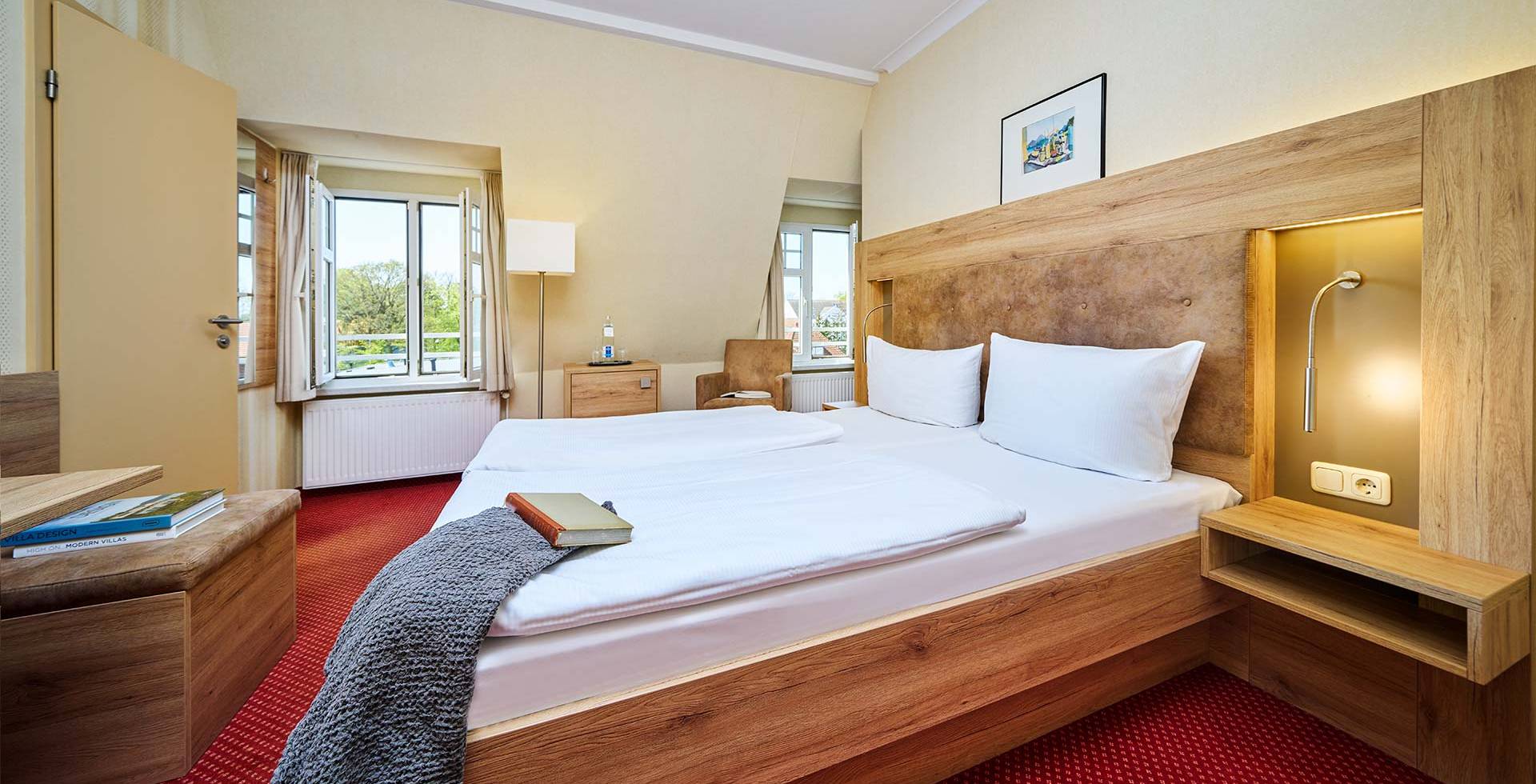 Doppelzimmer im Strandhotel Kormoran mit Ostseeblick, großem Bett, Schreibtisch, Sessel und Nachttischlampen.