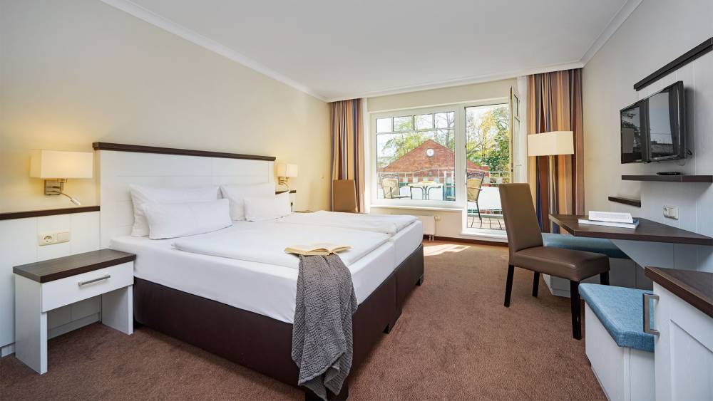 Economy Doppelzimmer im Strandhotel Luise mit Bett, Schreibtisch, TV, Stuhl und großem Fenster.