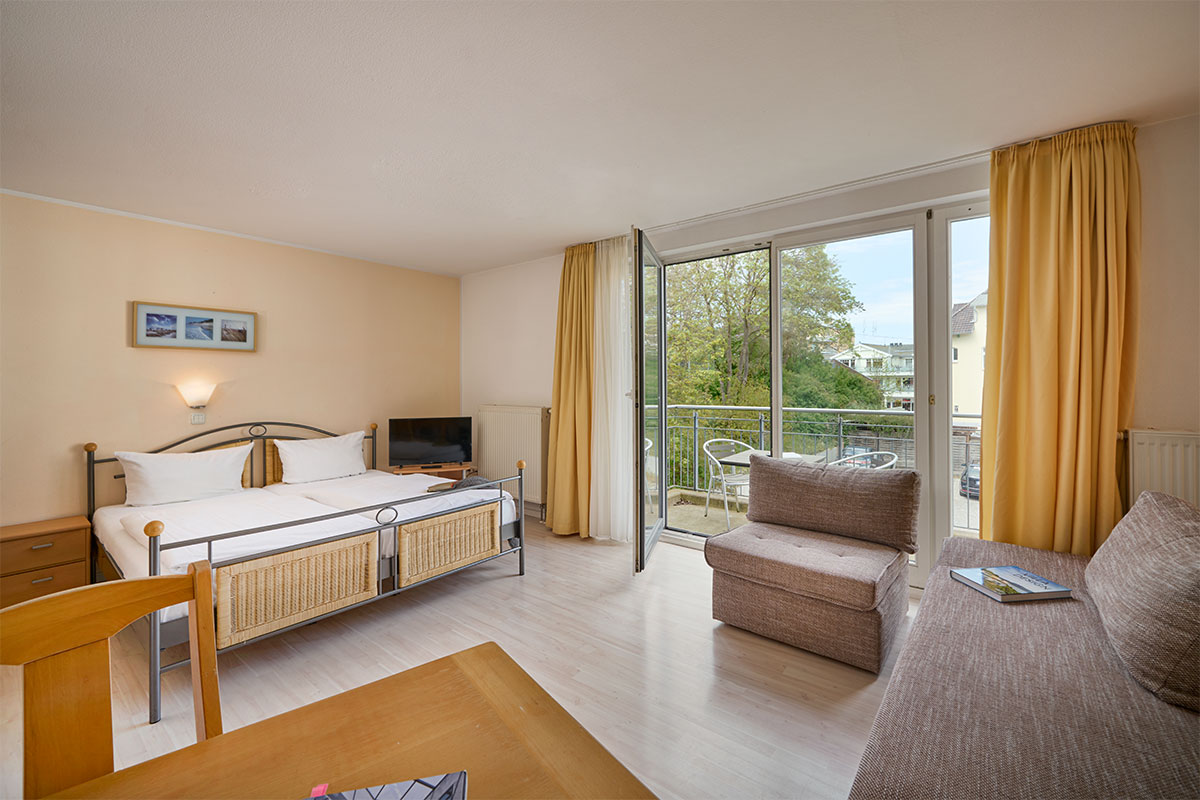 Helles, gut ausgestattetes Wohnzimmer des Ferienapartments Strandperle mit Doppelbett, Sofa und Balkon.