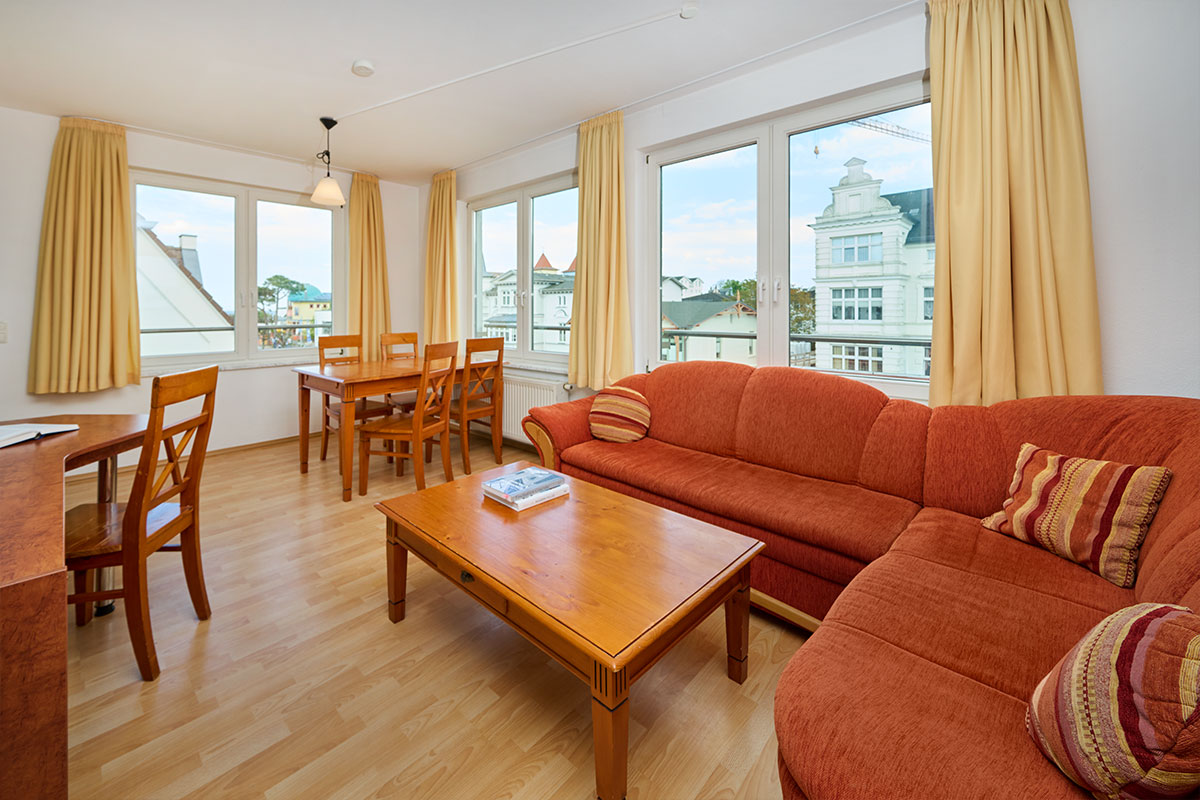 Freundlicher Wohnbereich mit großem Sofa, Esstisch und Balkonzugang in den Ferienwohnungen auf Usedom.