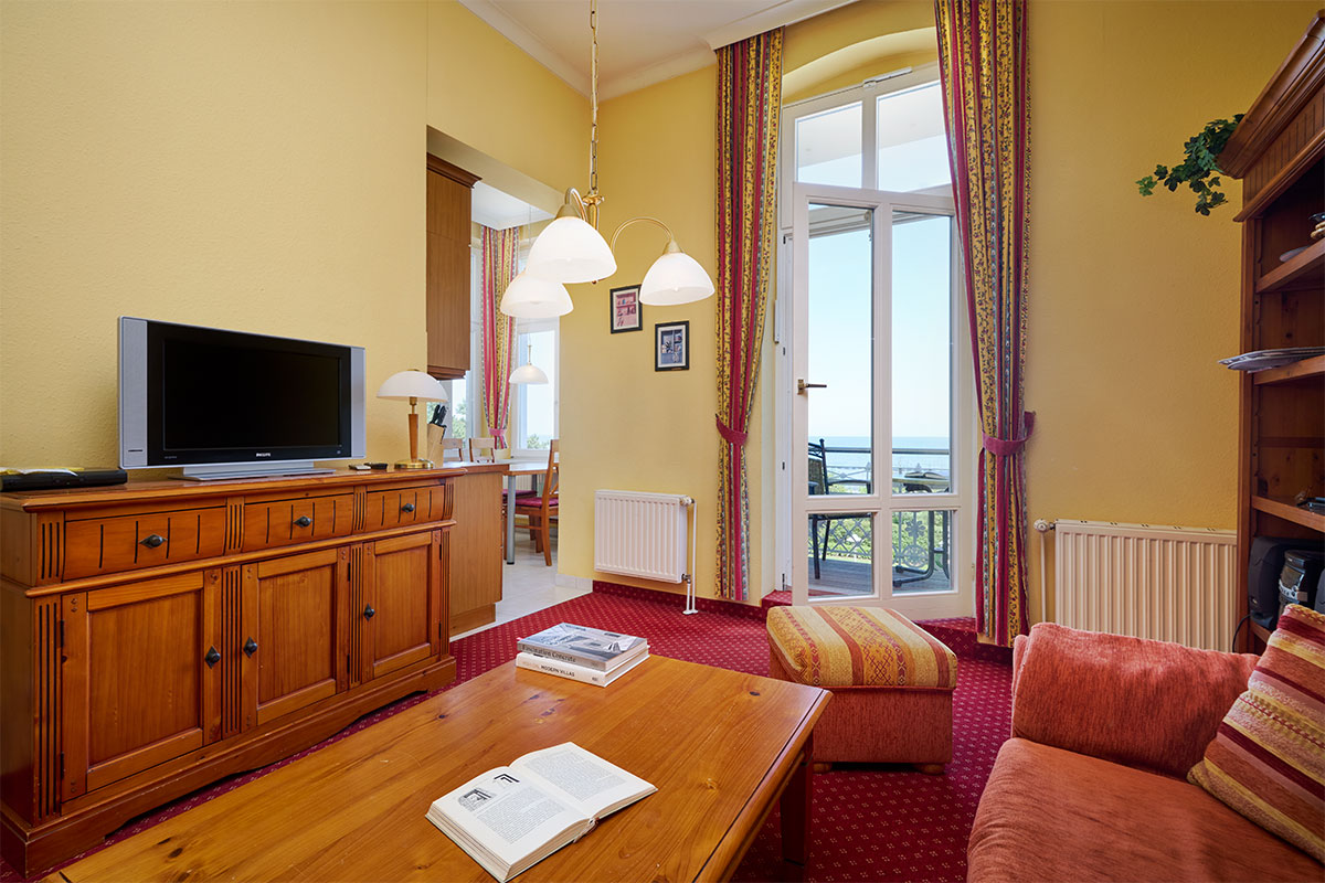 Wohnbereich mit Sofa, TV und Balkon mit Meerblick in den Ferienwohnungen der Strandvillen Wald und See auf Usedom.