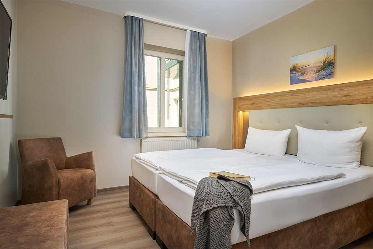 Schlafzimmer mit Doppelbett, Sessel und Fenster in der Familiensuite zur Landseite auf Usedom.