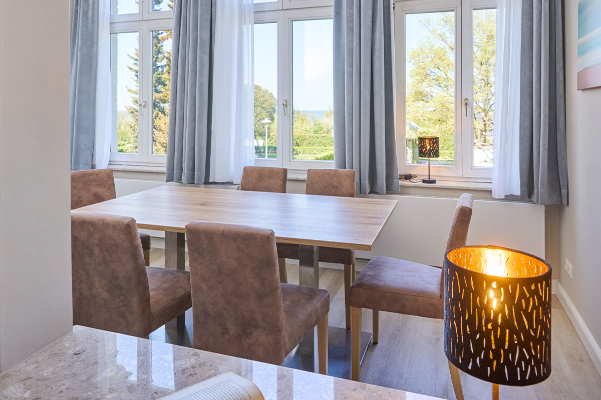 Essbereich mit sechs Stühlen, einer Lampe und großen Fenstern in einer Familiensuite auf Usedom.