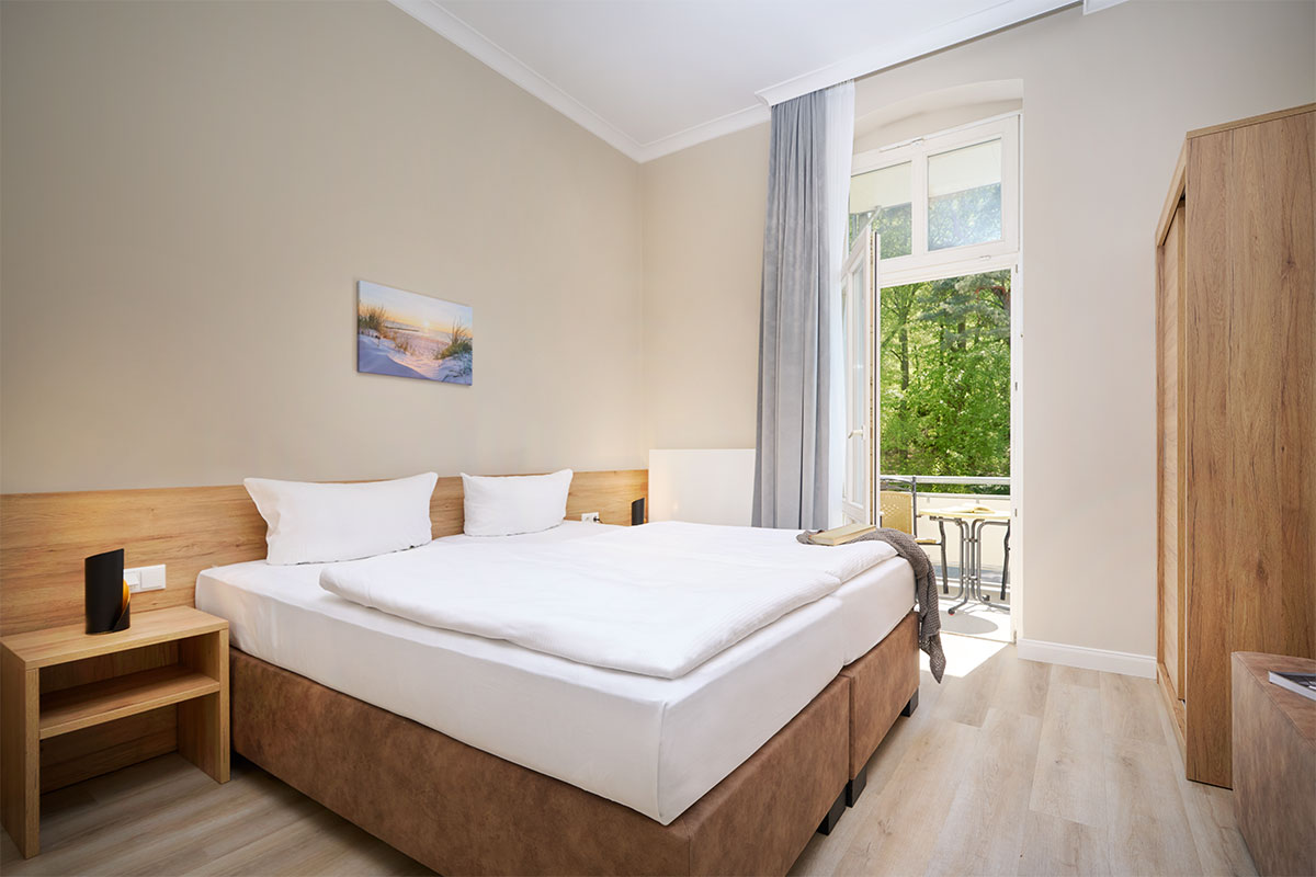 Schlafzimmer mit Doppelbett und Balkonzugang in der Familiensuite zur Meerseite an der Ostsee.