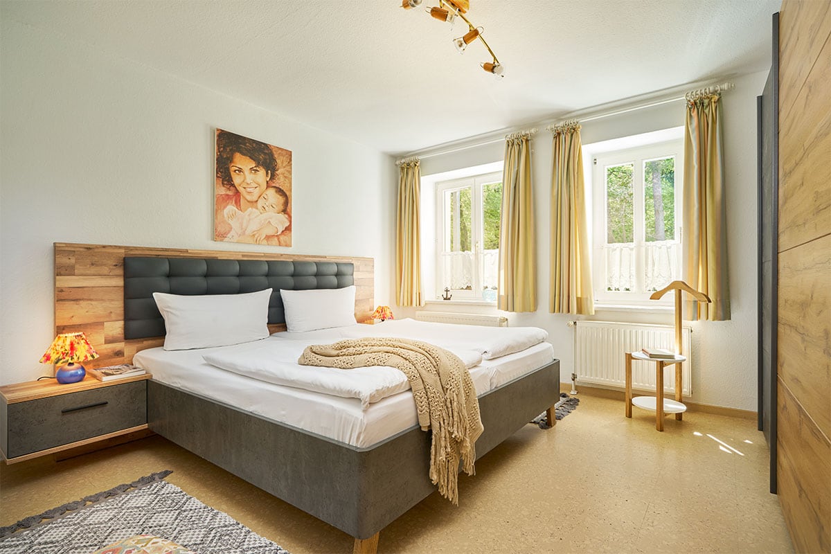 Schlafzimmer mit Doppelbett, Fenstern und warmen Farben in der Juniorsuite der Strandvillen Wald und See.