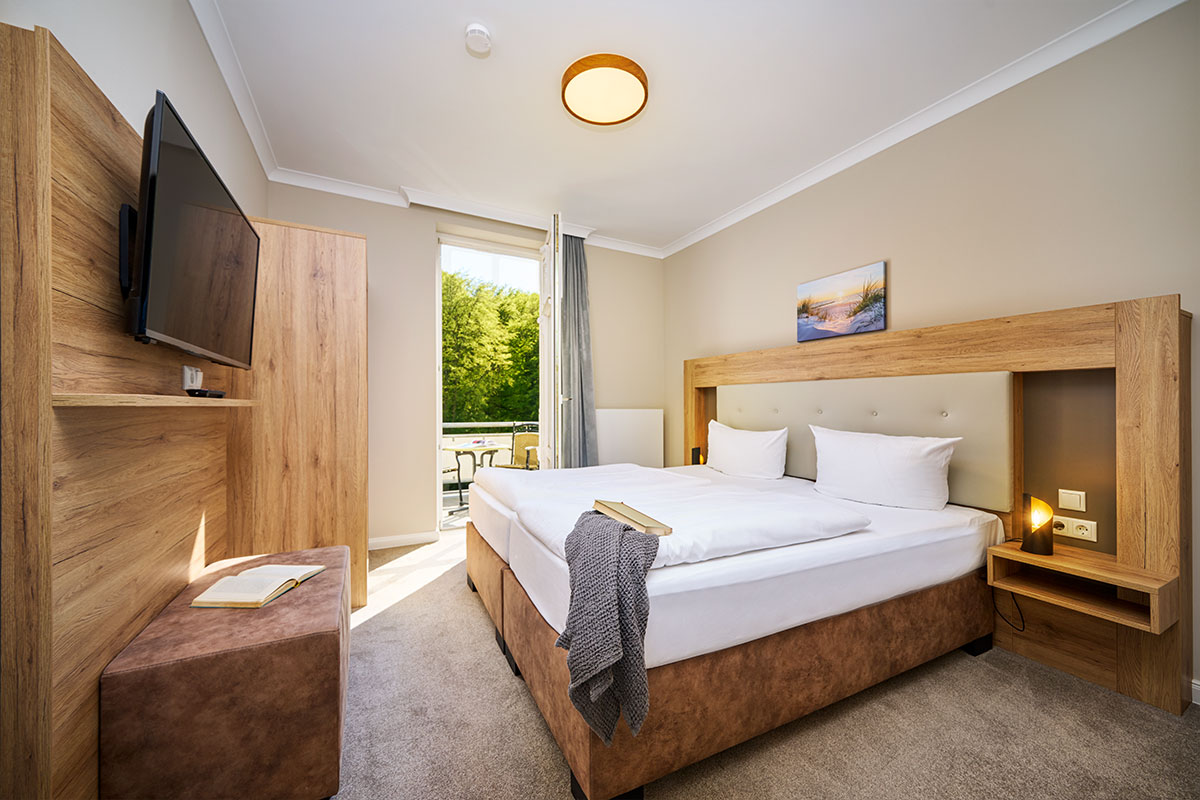 Schlafzimmer mit Doppelbett, Balkonzugang und TV in einer Suite mit Panorama-Meerblick auf Usedom.