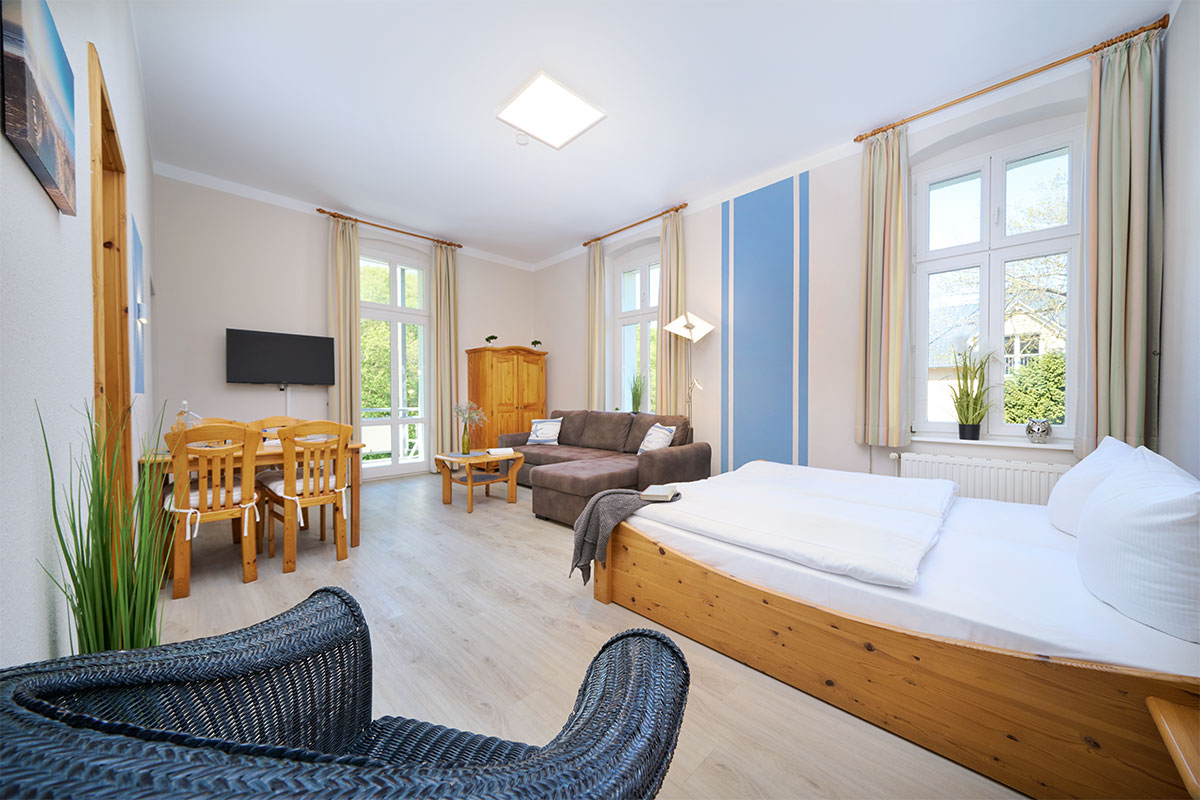 Heller Wohn- und Schlafbereich im Studio Apartment zur Landseite mit Esstisch, Sofa und großem Fenster.