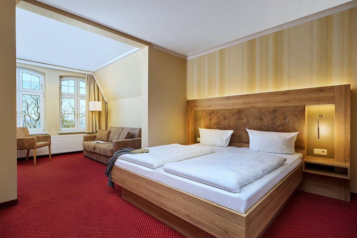 Gemütliches Doppelzimmer mit Sitzbereich und großen Fenstern im Strandhotel Garni Kormoran an der Ostsee.