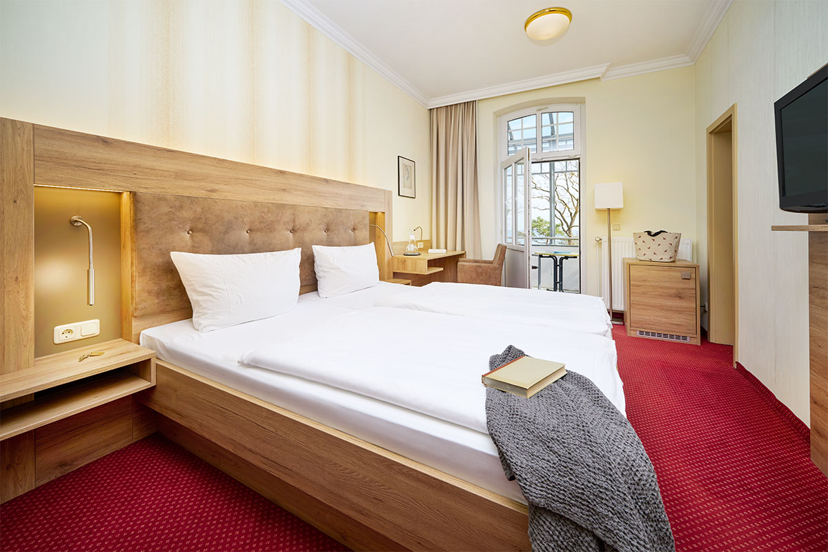 Doppelzimmer mit Bett, TV, Schreibtisch, Sessel und Fenster mit Blick zur Ostsee.