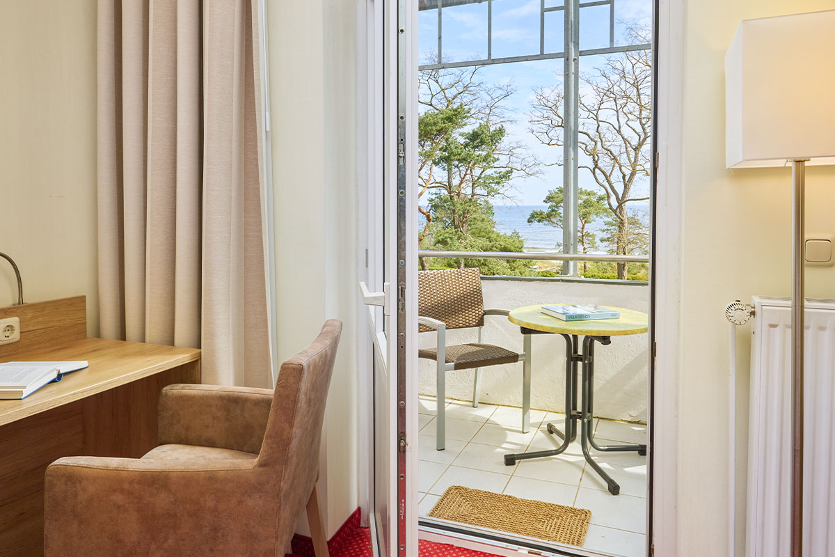 Balkon im Strandhotel Kormoran mit Stühlen, Tisch, Meerblick, Schreibtisch und Sessel im Vordergrund.