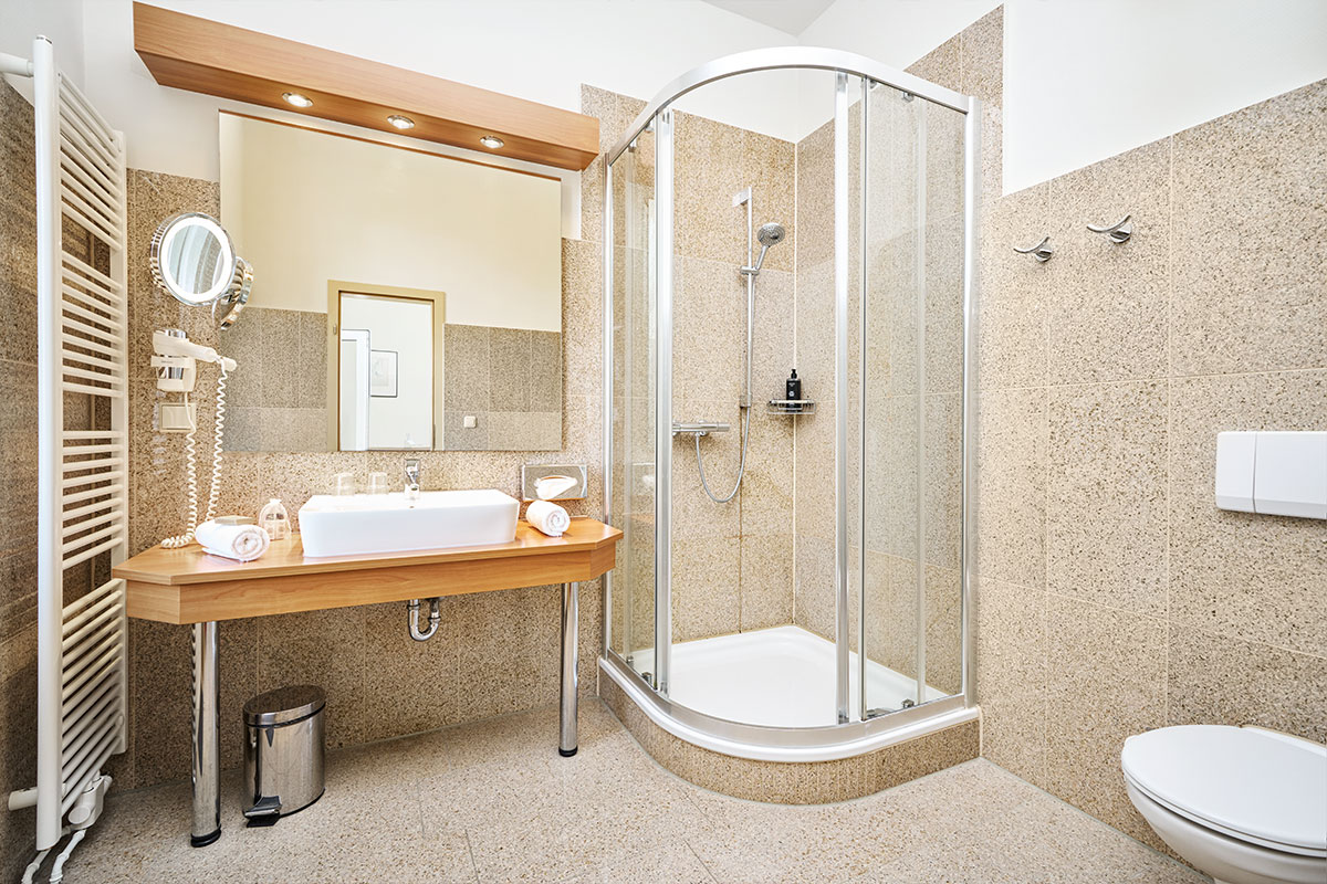 Modernes Badezimmer im Strandhotel Kormoran mit Dusche, WC, Waschbecken, Spiegel und Kosmetikspiegel.