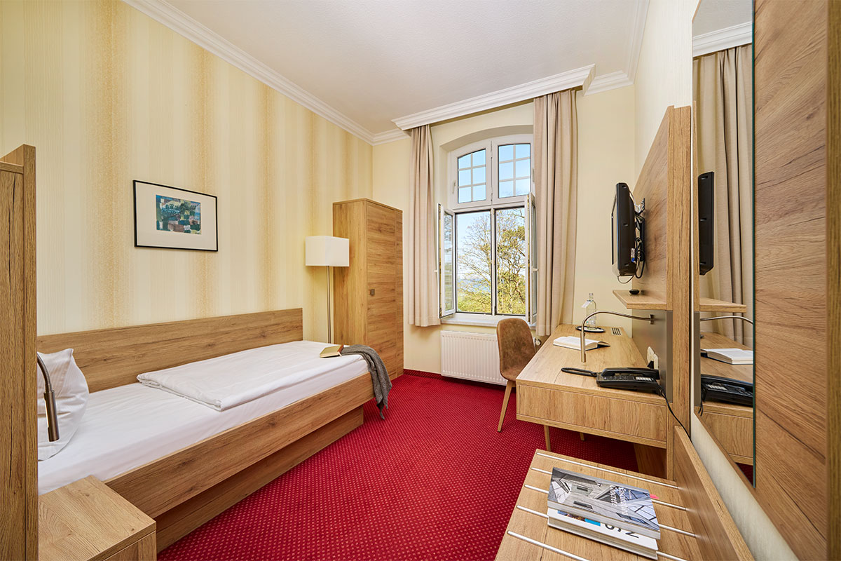 Einzelzimmer im Strandhotel Kormoran mit Schreibtisch, Spiegel, Fernseher und Fenster mit Blick zur Ostsee.
