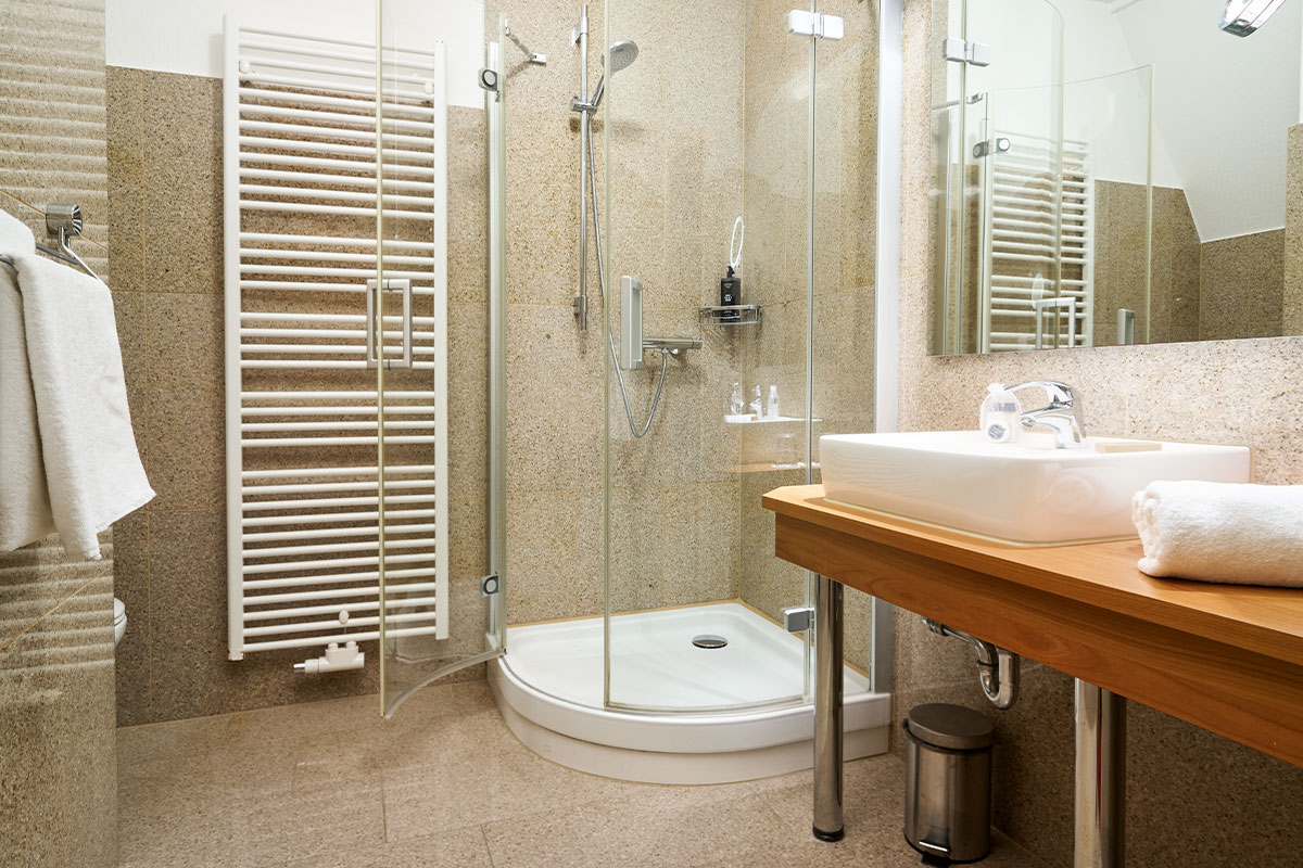 Badezimmer mit Glasdusche, Waschbecken, Handtuchheizung und Spiegel im Strandhotel Kormoran auf Usedom.