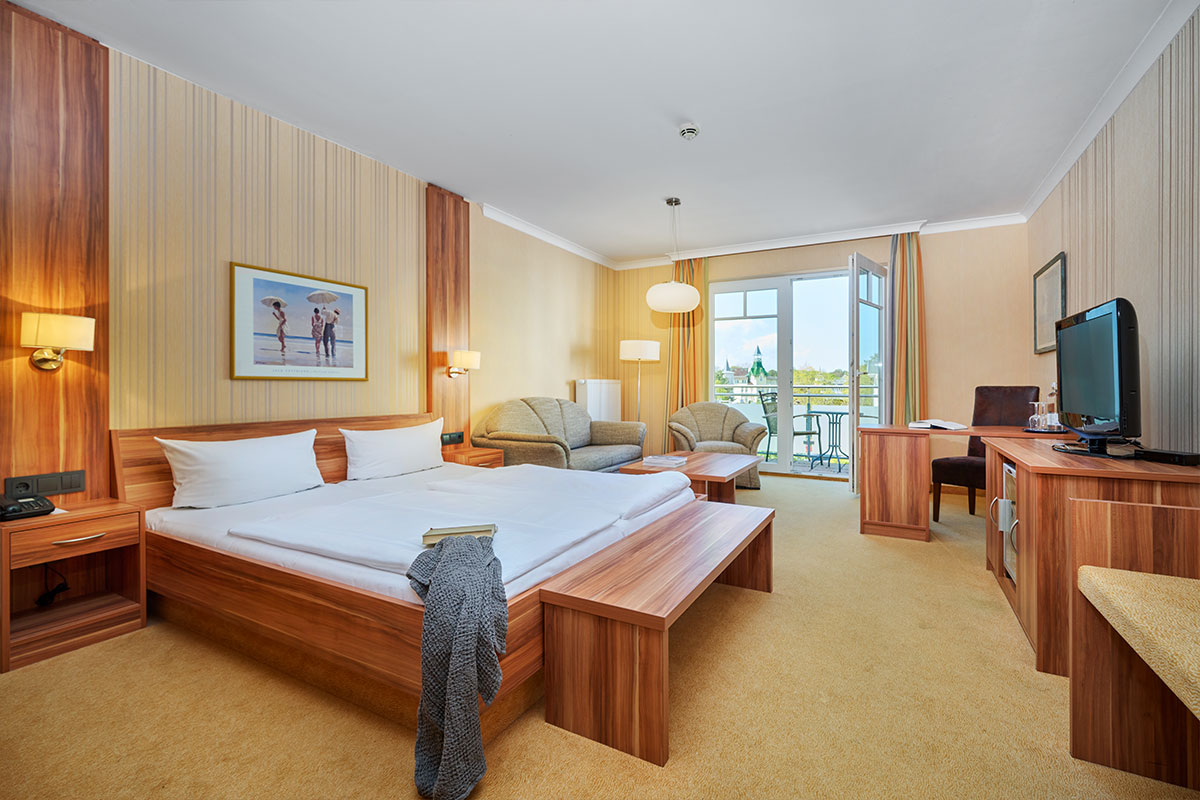 Komfortzimmer mit Doppelbett, Sofa, Schreibtisch, Fernseher und Balkon im Strandhotel garni Kormoran.