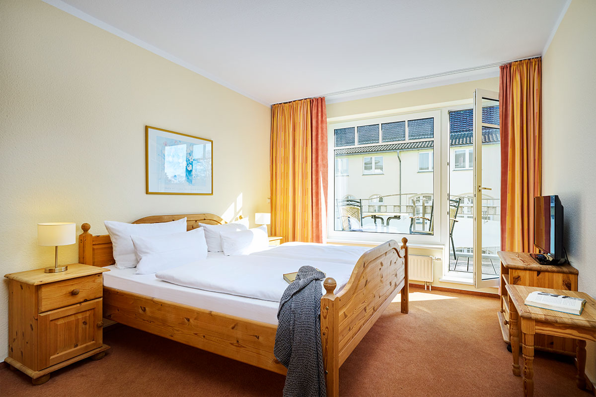 Helles Schlafzimmer mit Doppelbett, Nachttischen, TV und Zugang zum Balkon im Strandhotel Luise auf Usedom.