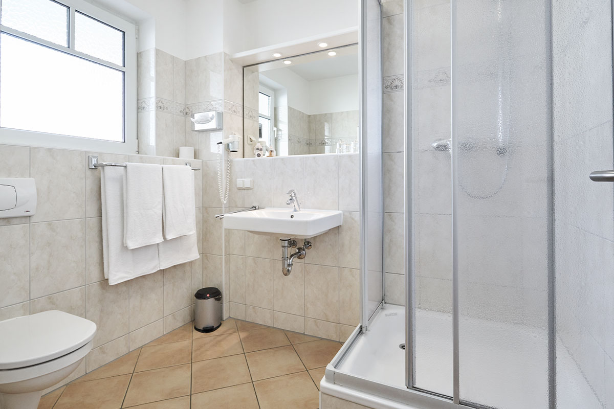 Helles Bad im Economy Doppelzimmer des Strandhotel Luise mit Dusche, WC, Waschbecken und Spiegel.