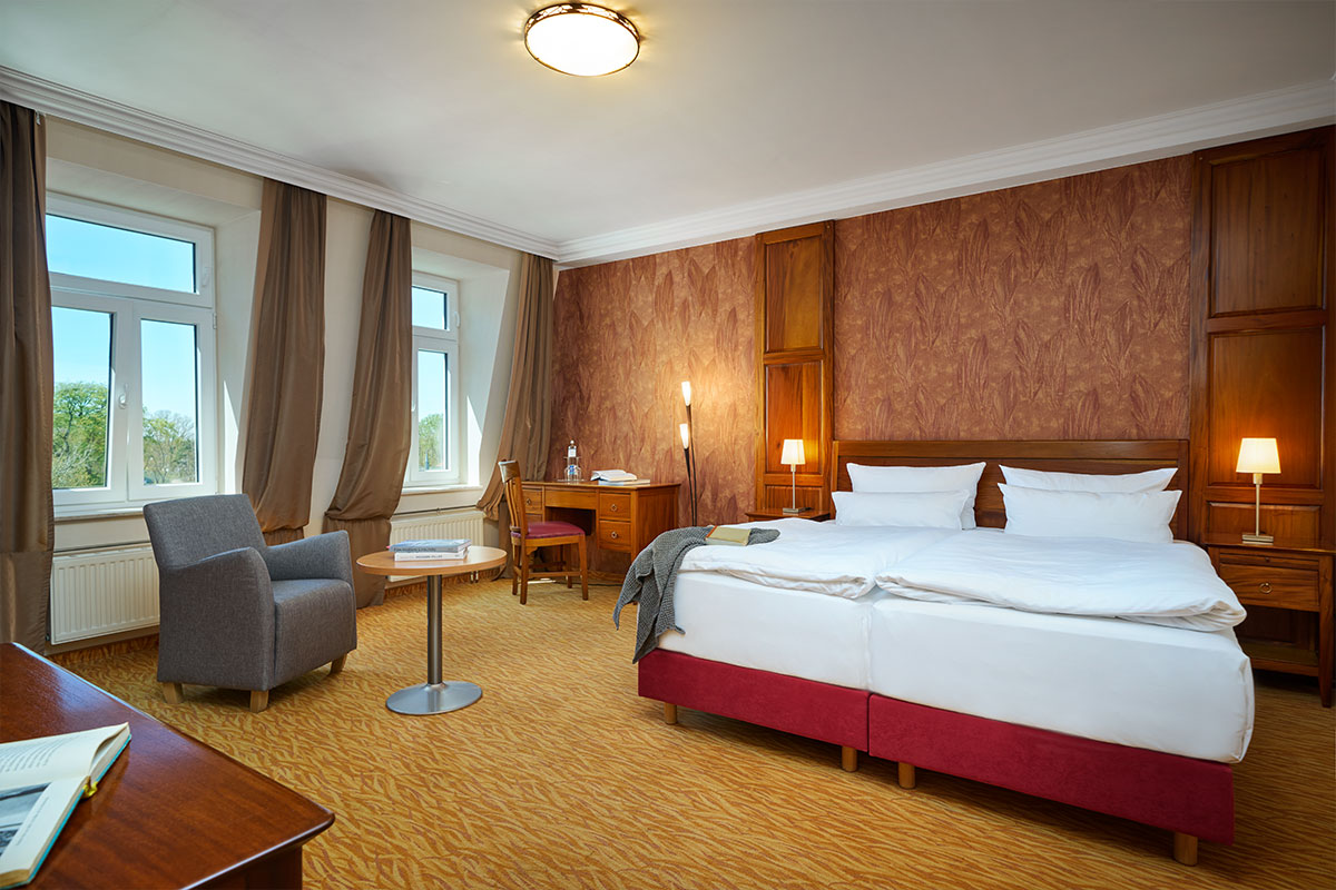 Doppelzimmer im Strandhotel Preußenhof mit großem Bett, Sesseln, Schreibtisch, Fenstern und Teppich.