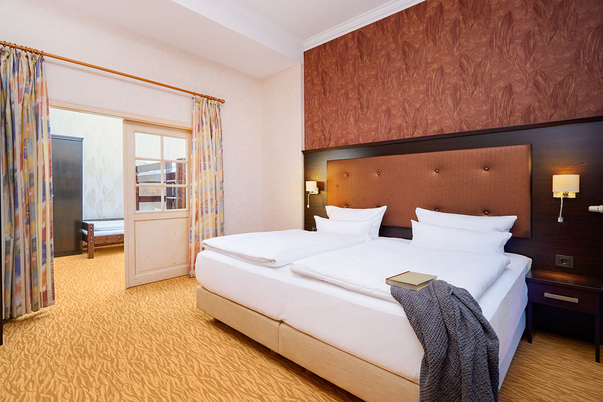 Hauptschlafzimmer mit Doppelbett, Nachttischlampen und Blick ins Kinderzimmer im Strandhotel Preußenhof.