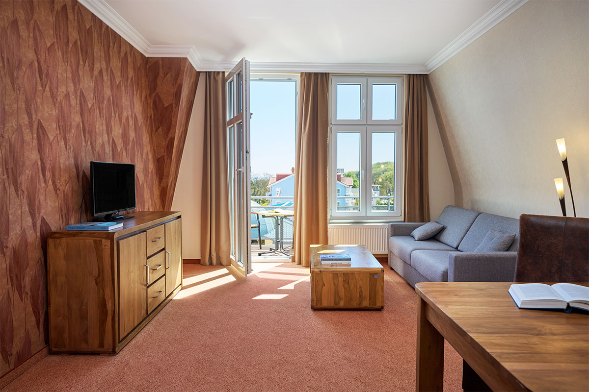 Junior Suite mit Couch, TV, Tisch und Balkon im Strandhotel Preußenhof mit Blick auf die Ostsee.