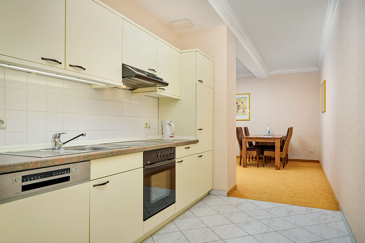 Küche mit Herd, Backofen, Spüle, Wasserkocher und Blick in den Essbereich im Strandhotel Preußenhof an der Ostsee.