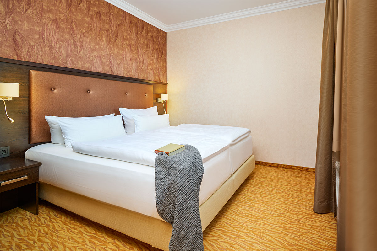 Schlafzimmer mit Doppelbett, Nachttischen, Wandlampen und Fenster zur Landseite im Strandhotel Preußenhof.