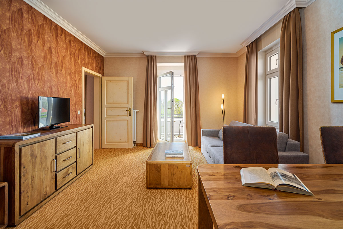 Wohnzimmer mit Sofa, Fernseher, Tisch und Zugang zum Balkon im Strandhotel Preußenhof auf Usedom.