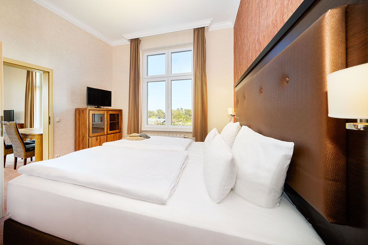 Turm Suite im Strandhotel Preußenhof mit Doppelbett, TV, Fenster und Verbindung zum Wohnbereich.