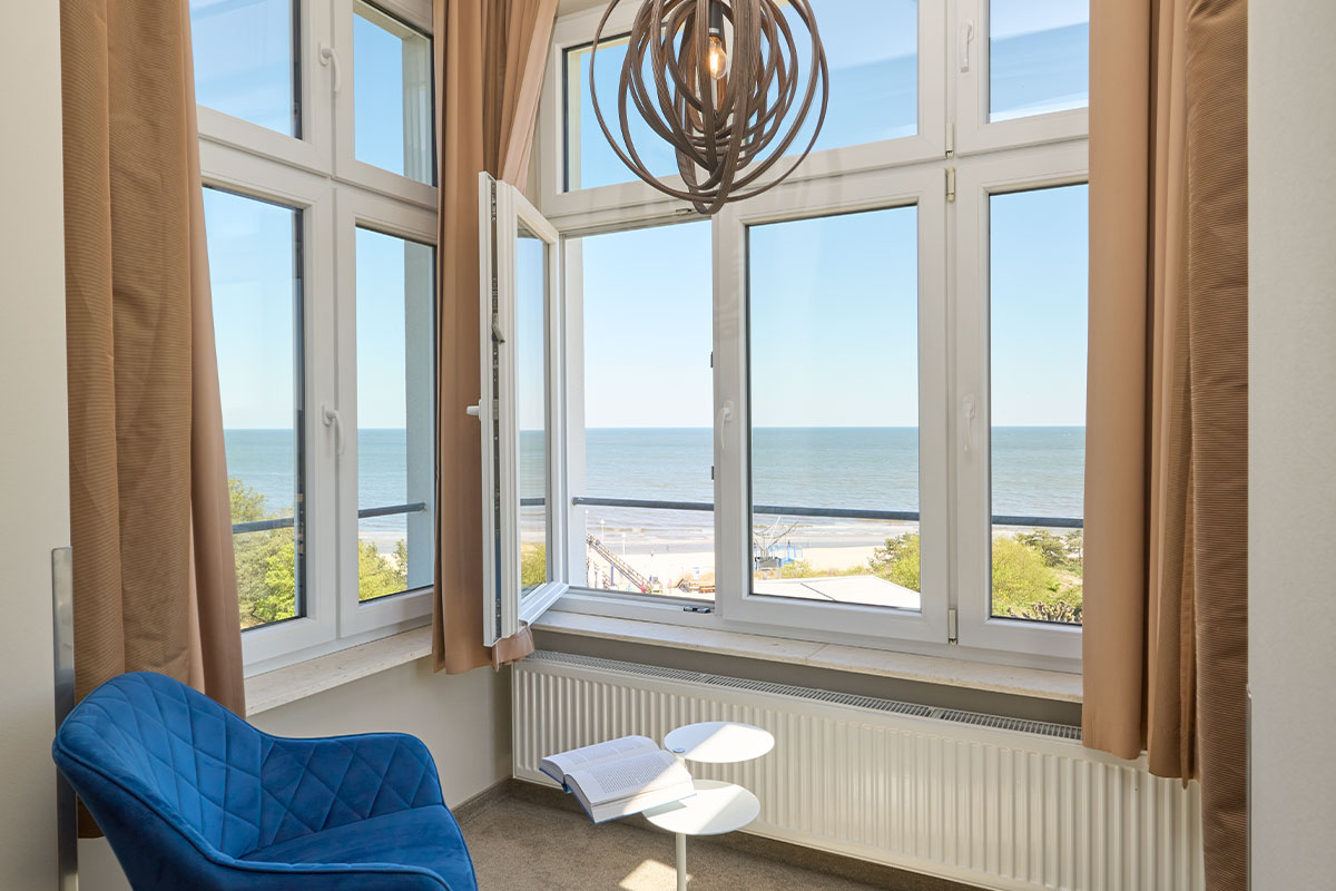 Sitzecke mit blauem Sessel, Tisch und großem Fenster mit Blick auf die Ostsee.