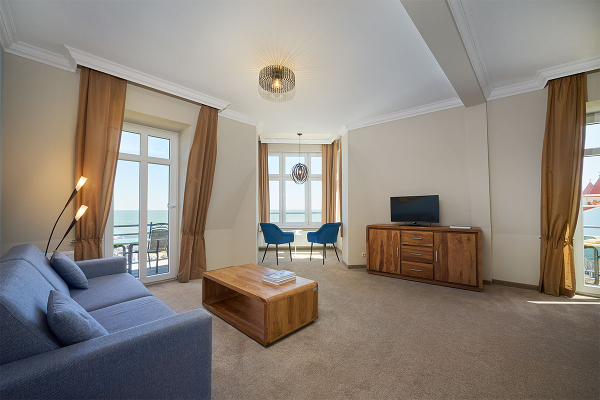 Turm Suite mit Sofa, TV, Couchtisch, Sesseln, Balkon und Panoramablick auf die Ostsee.