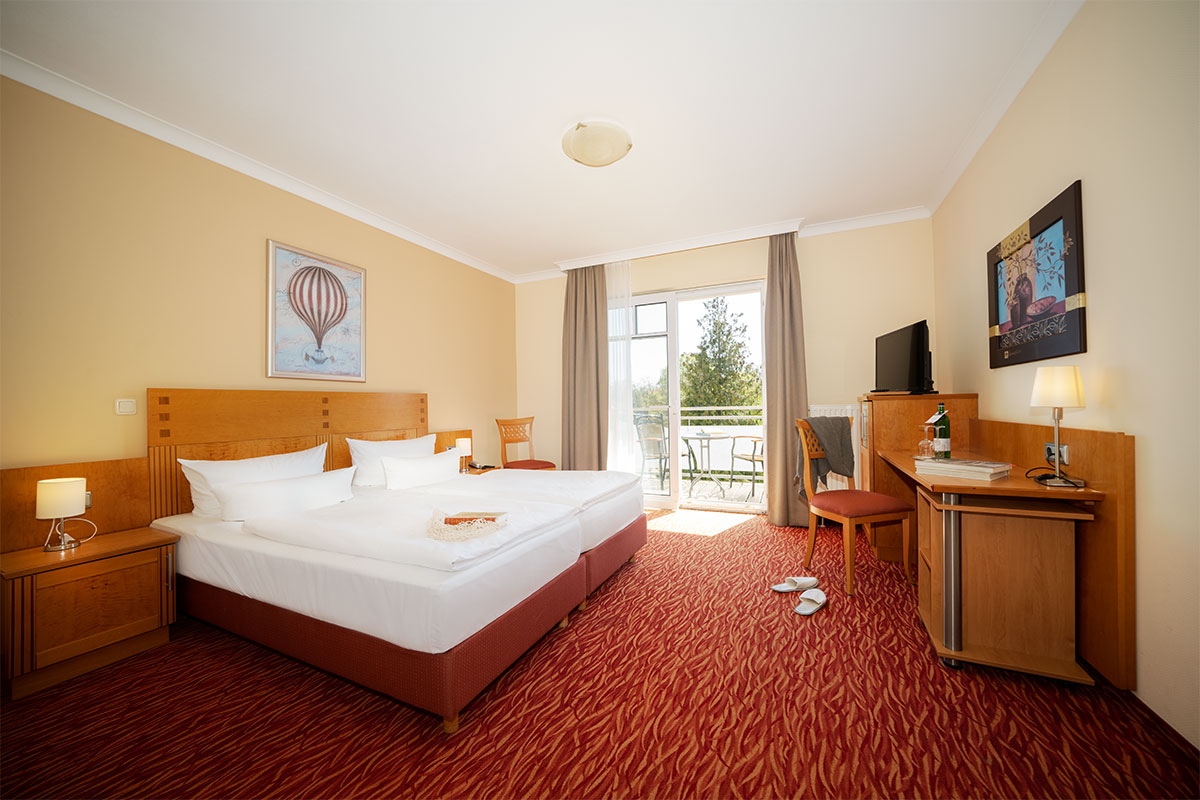 Porträt eines gemütlichen Doppelzimmers mit Teppichboden, Balkonmöbeln und Tageslicht im Strandhotel Prinz von Preussen.
