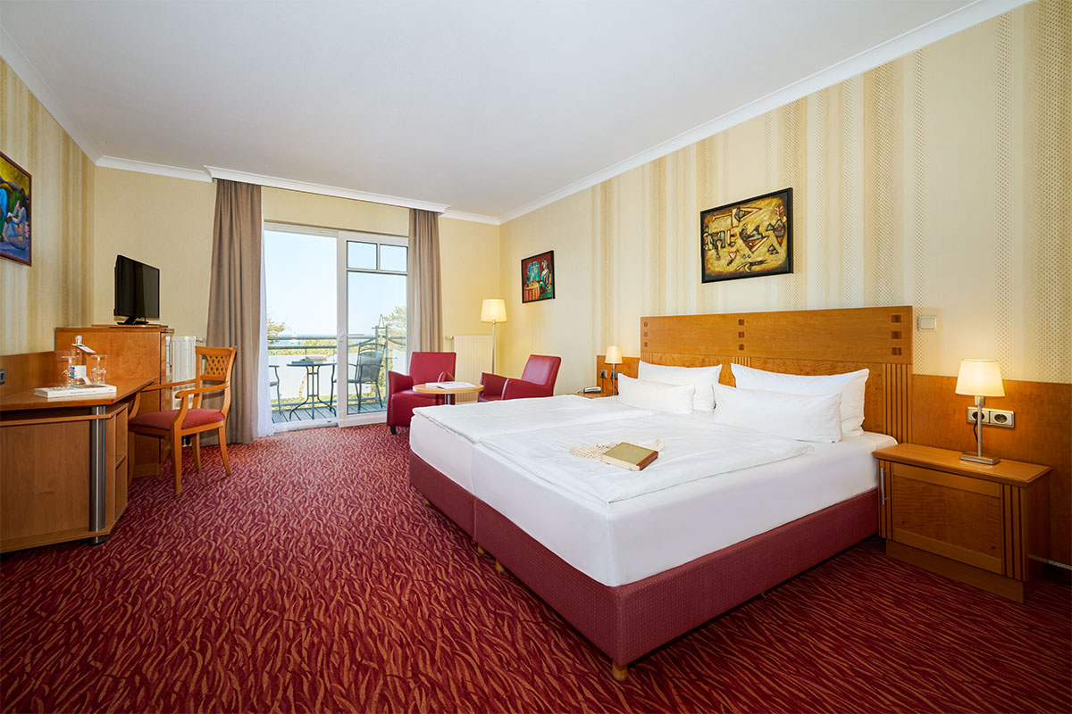 Porträt eines lichtdurchfluteten Doppelzimmers im Strandhotel Prinz von Preussen mit Balkon und Aussicht aufs Meer.