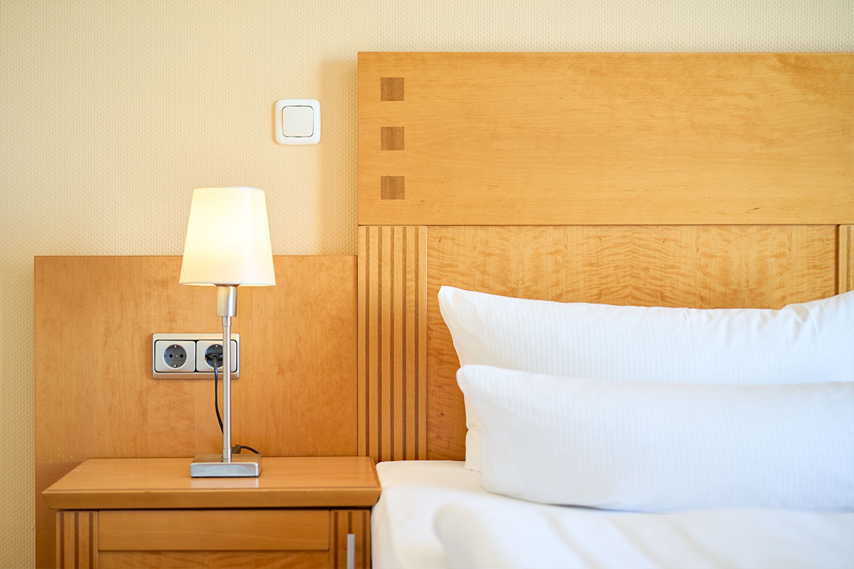 Doppelbett im Doppelzimmer Landseite mit weißer Bettwäsche, Holzrückwand, Nachttischlampe im Strandhotel Prinz von Preussen.