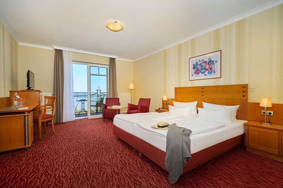 Porträt vom Hotelzimmer mit Balkonblick auf die Ostsee, gemütlichem Bett, Minibar, Sesseln im Strandhotel Prinz von Preussen