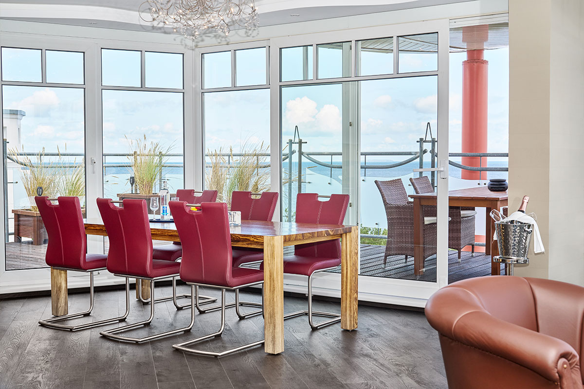 Esstisch im Penthouse des Strandhotel Prinz von Preussen von Schöner Inseln mit roten Stühlen und Panoramablick auf die Ostsee.