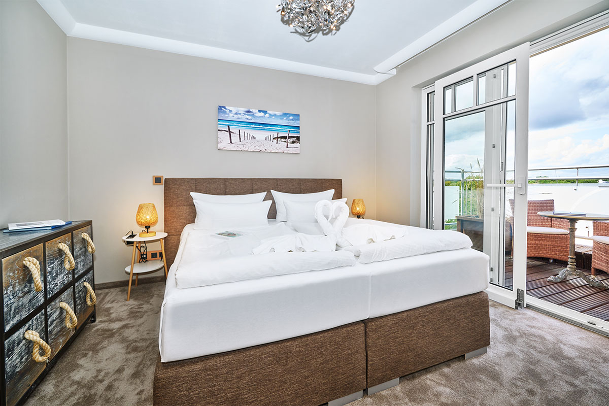 Penthouse-Schlafzimmer mit Boxspringbett, Glastüren zur Terrasse und gemütlicher Einrichtung im Strandhotel Prinz von Preussen.