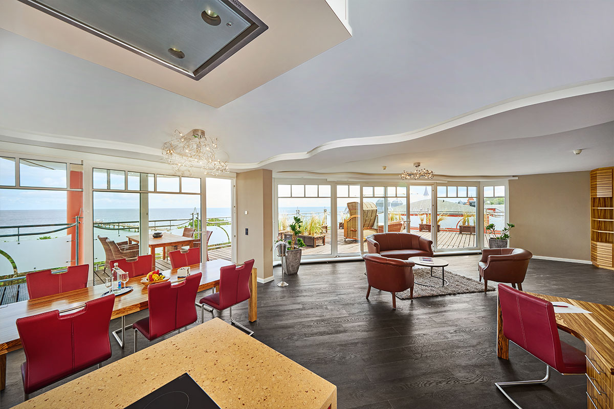 Großer Wohn-Essbereich im Penthouse des Strandhotel Prinz von Preussen mit Meerblick, Balkon und roten Stühlen.