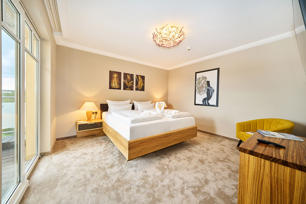 Schlafzimmer der Penthouse-Suite im Strandhotel Prinz von Preussen mit Doppelbett, Balkonzugang, Designmöbeln und Blick ins Grüne.