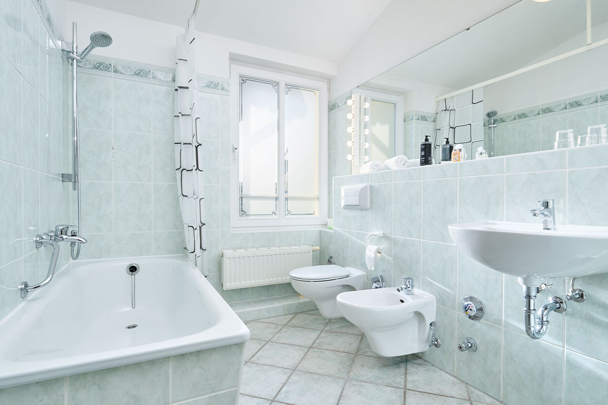 Helles Badezimmer im Doppelzimmer Landseite der Strandvilla Viktoria mit Badewanne, Bidet, Waschbecken und Fliesen.
