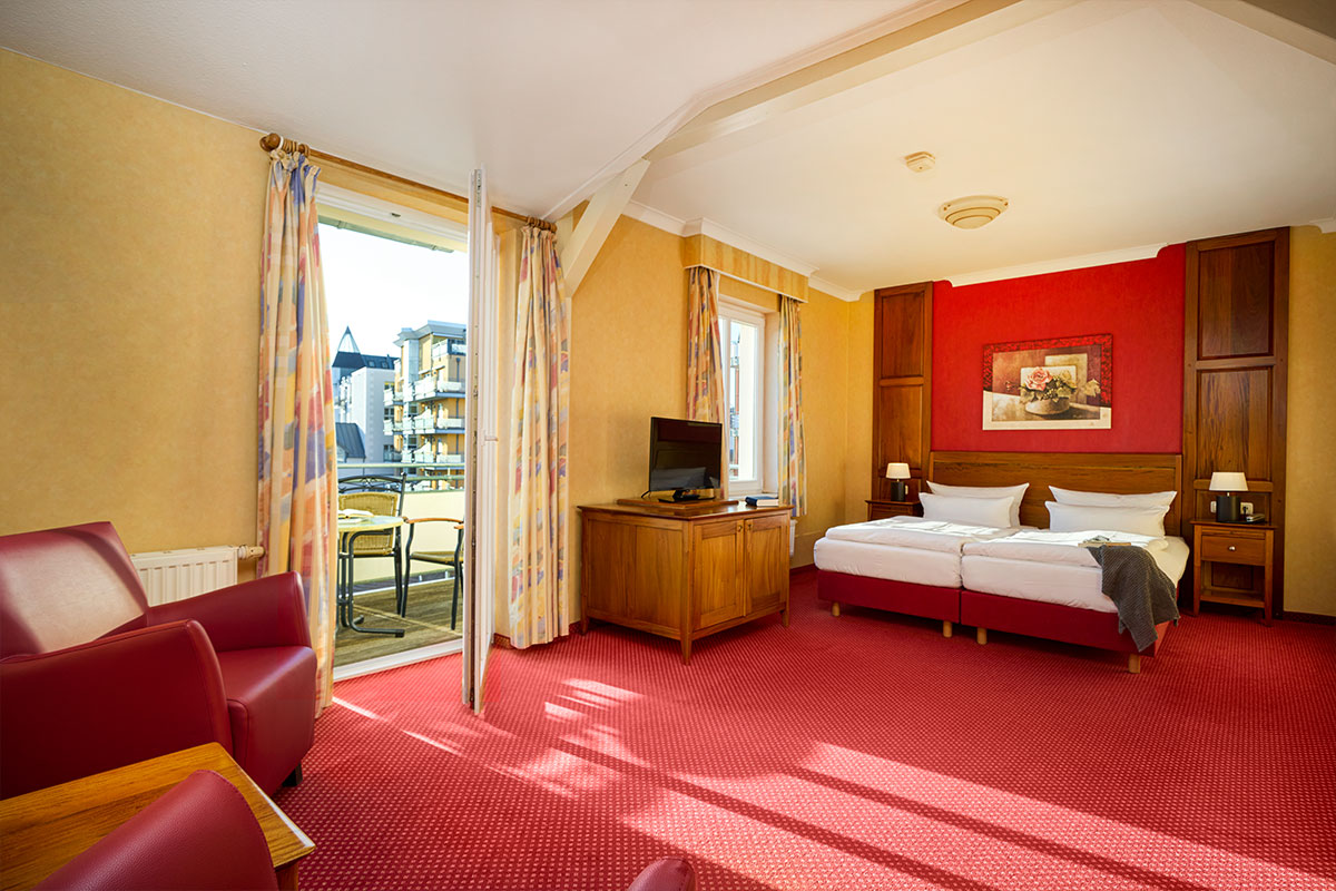 Doppelzimmer Landseite in der Strandvilla Viktoria auf Usedom mit zwei Betten, Sitzgruppe, Balkonzugang und warmem Teppichboden.